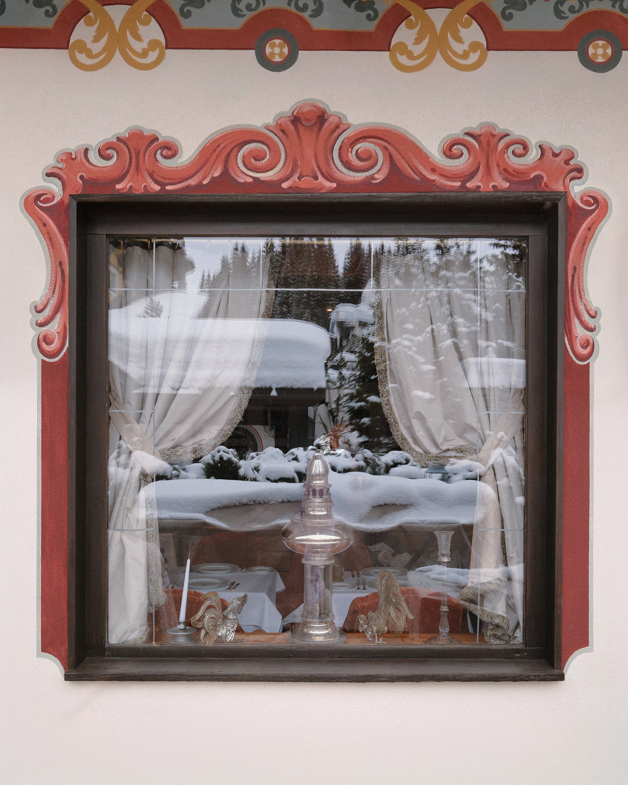 A window on the north face, silver roosters on the sill, the snow of the terrace held in the glass