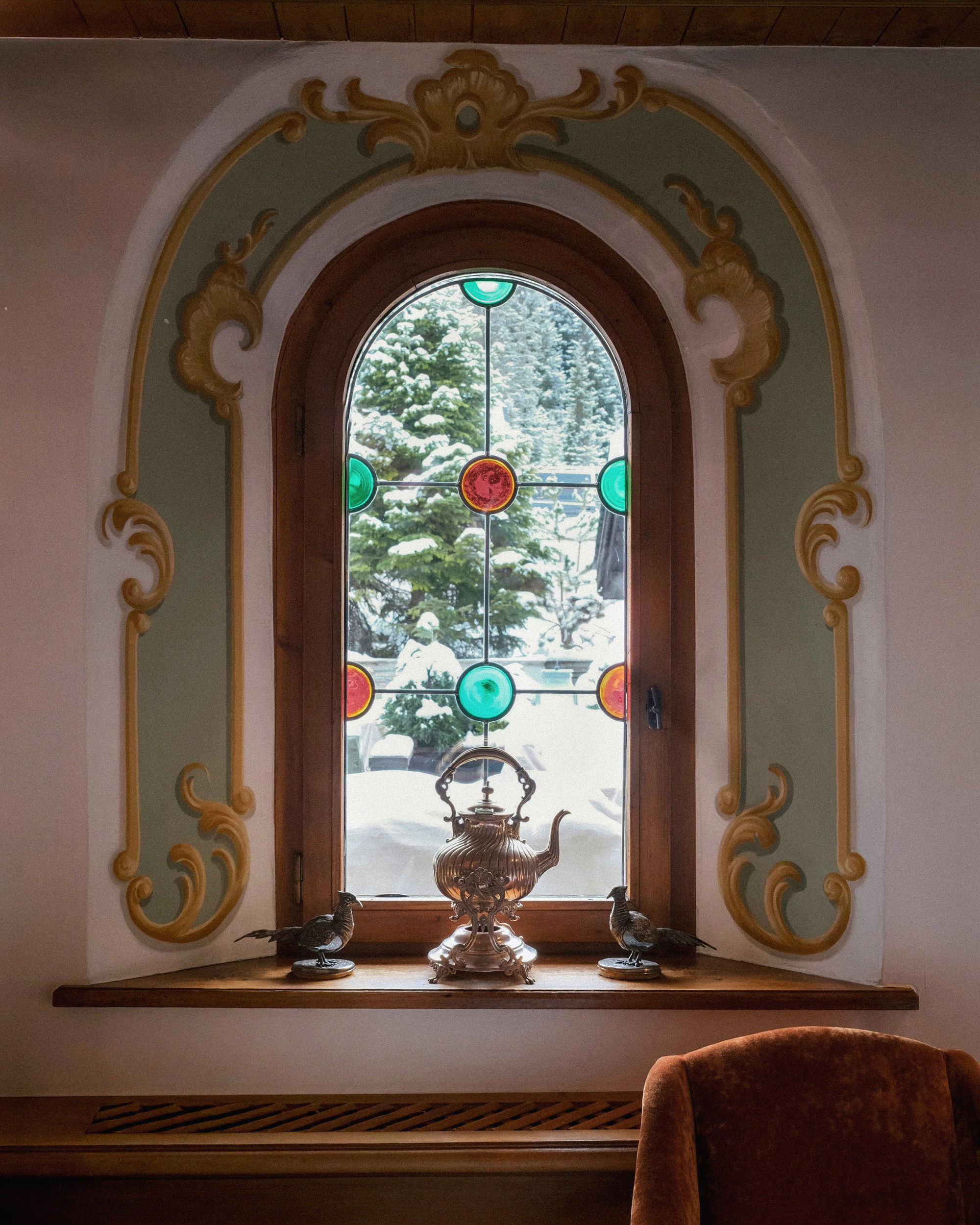 The samovar in the arched window, stained roundels, snow and spruce beyond the glass