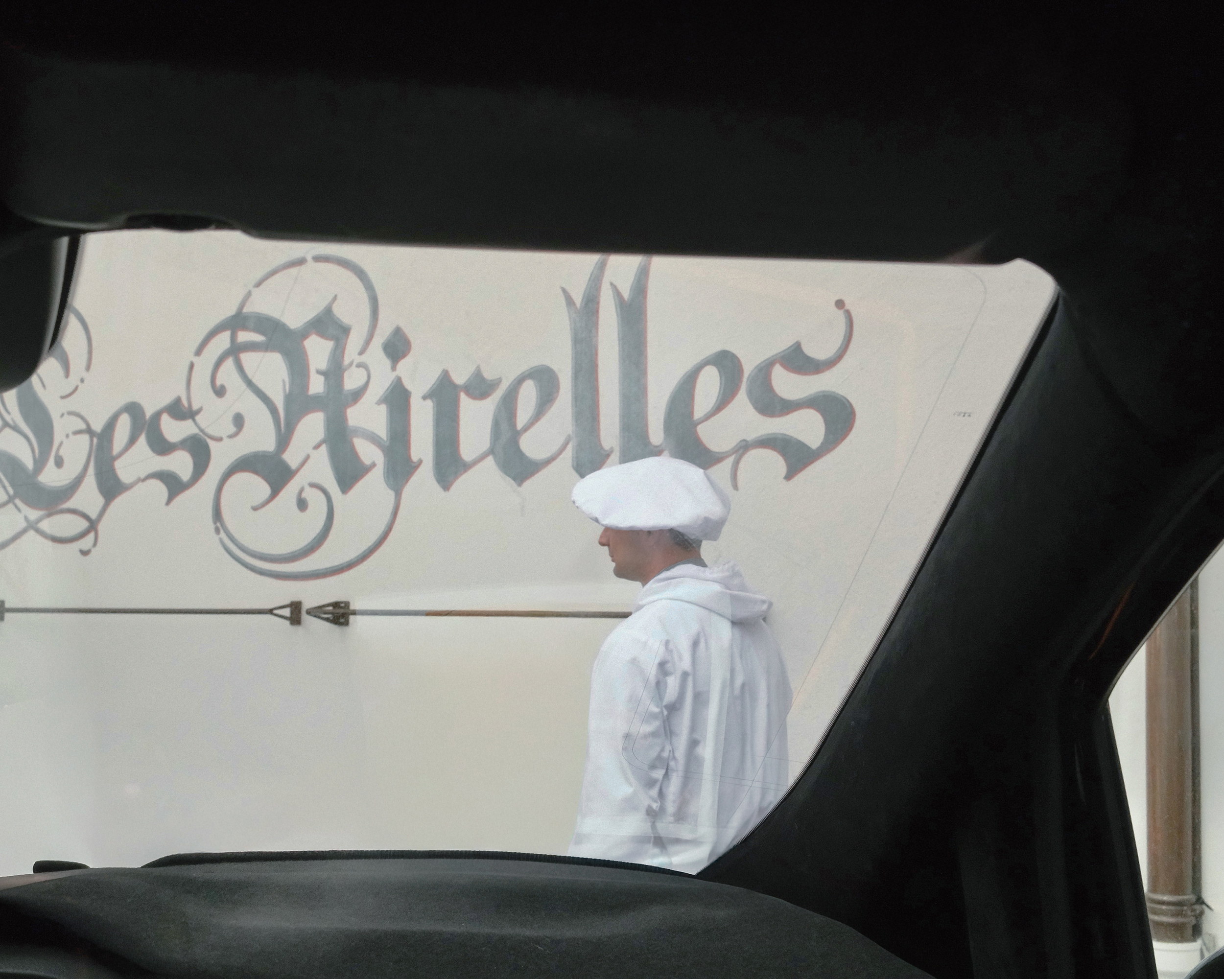 Les Airelles written on the wall, a chef in whites passing, the car door framing the departure