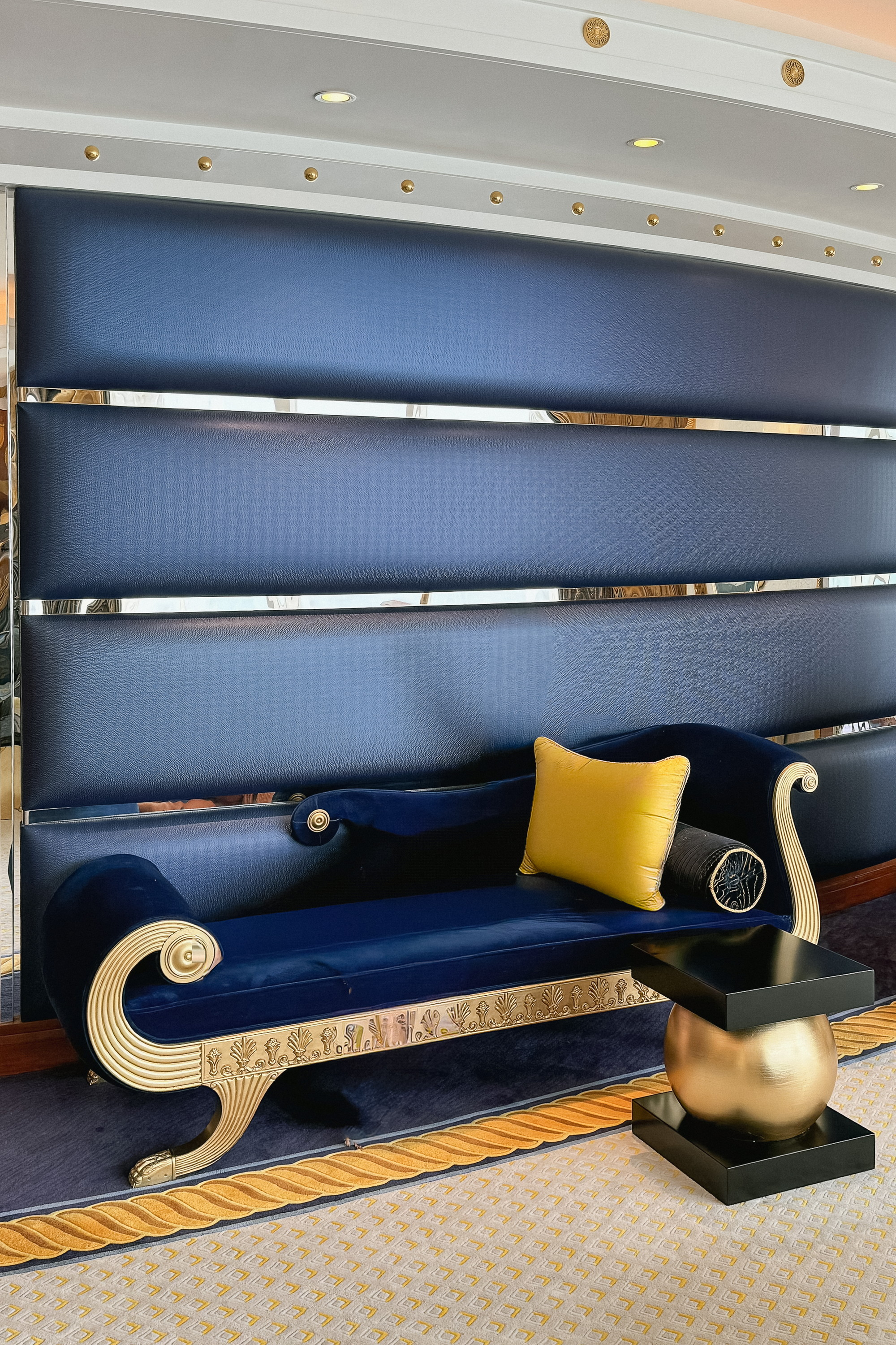 The gilded daybed against the navy wall, a yellow cushion