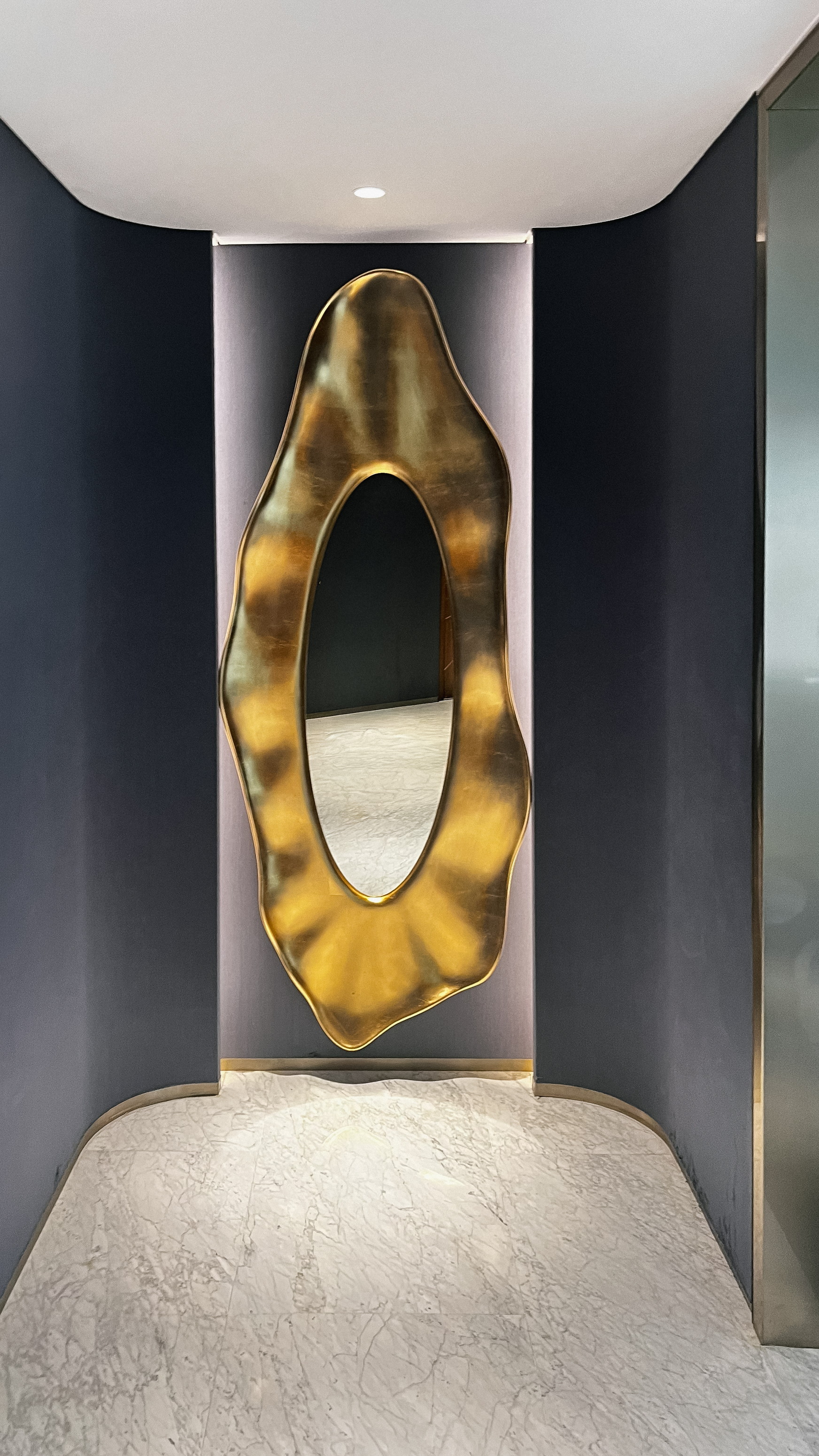 A gilded mirror in a navy niche, marble underfoot