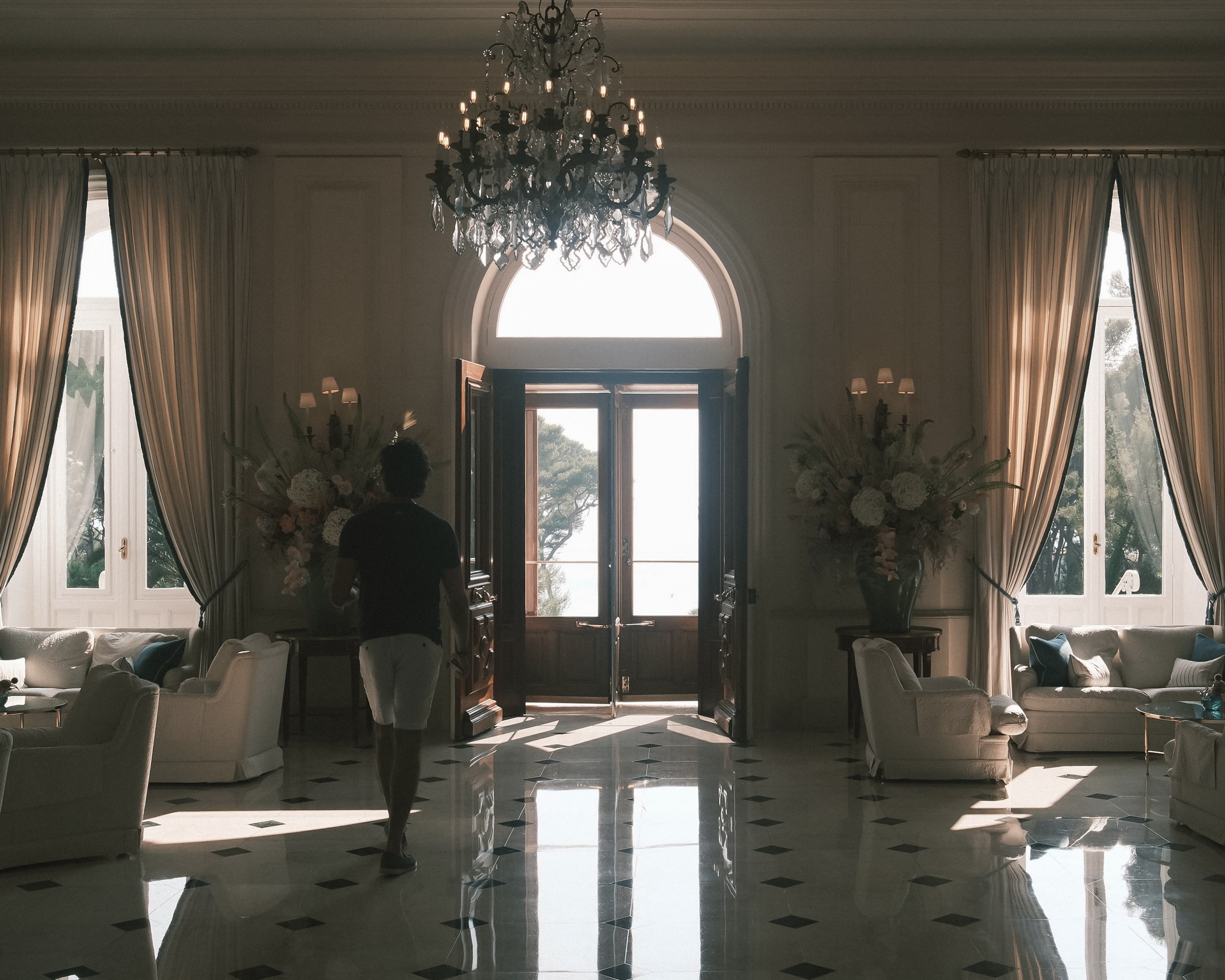 The grand salon at the shuttered hour, a figure passing through