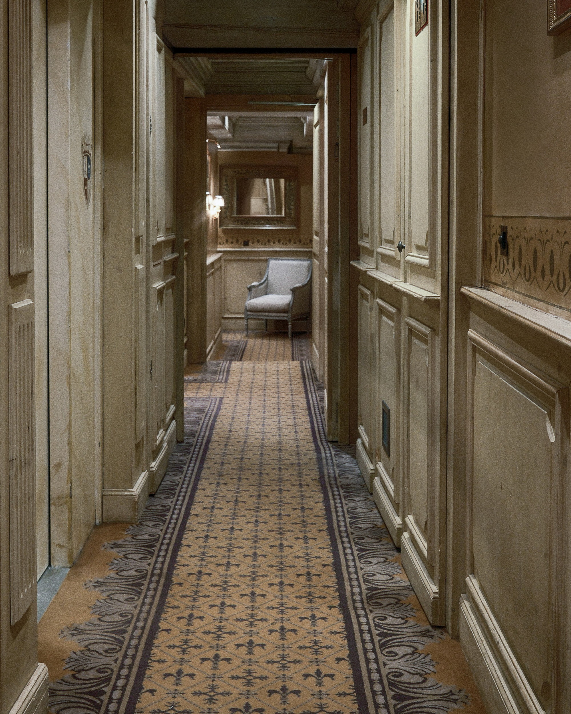 The corridor running to a chair and a mirror, fleur-de-lis on the runner