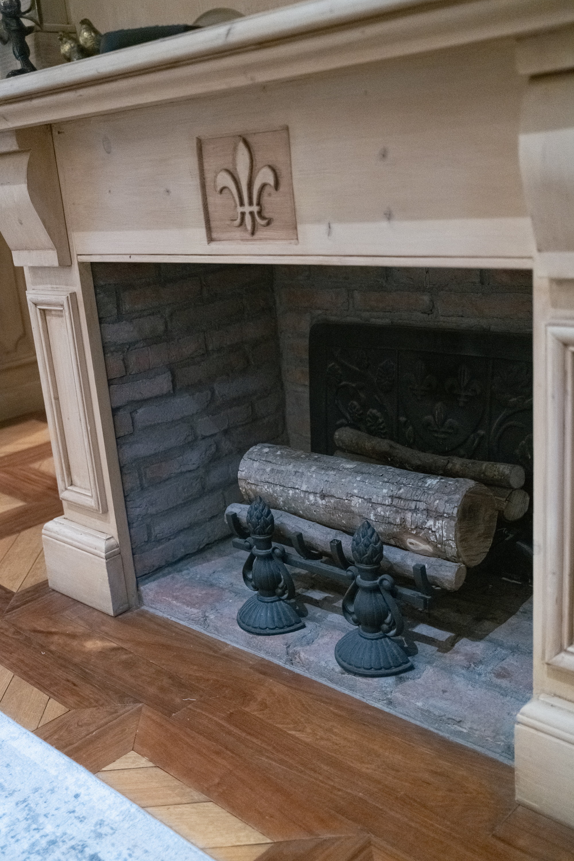 The hearth, a fleur-de-lis cut in the pine, andirons and a log
