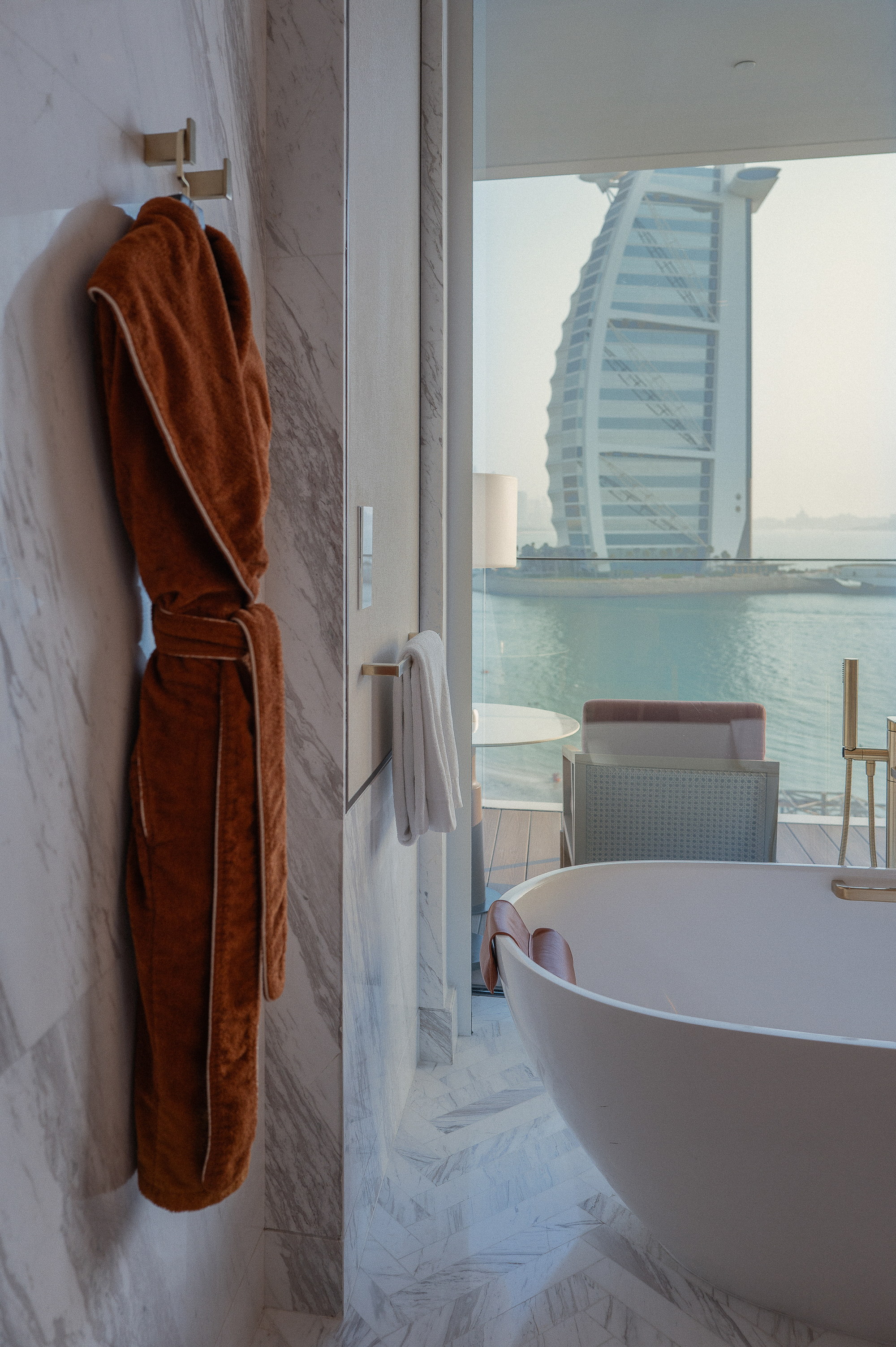 A robe on the hook, the bath at the glass, the Burj standing in the window