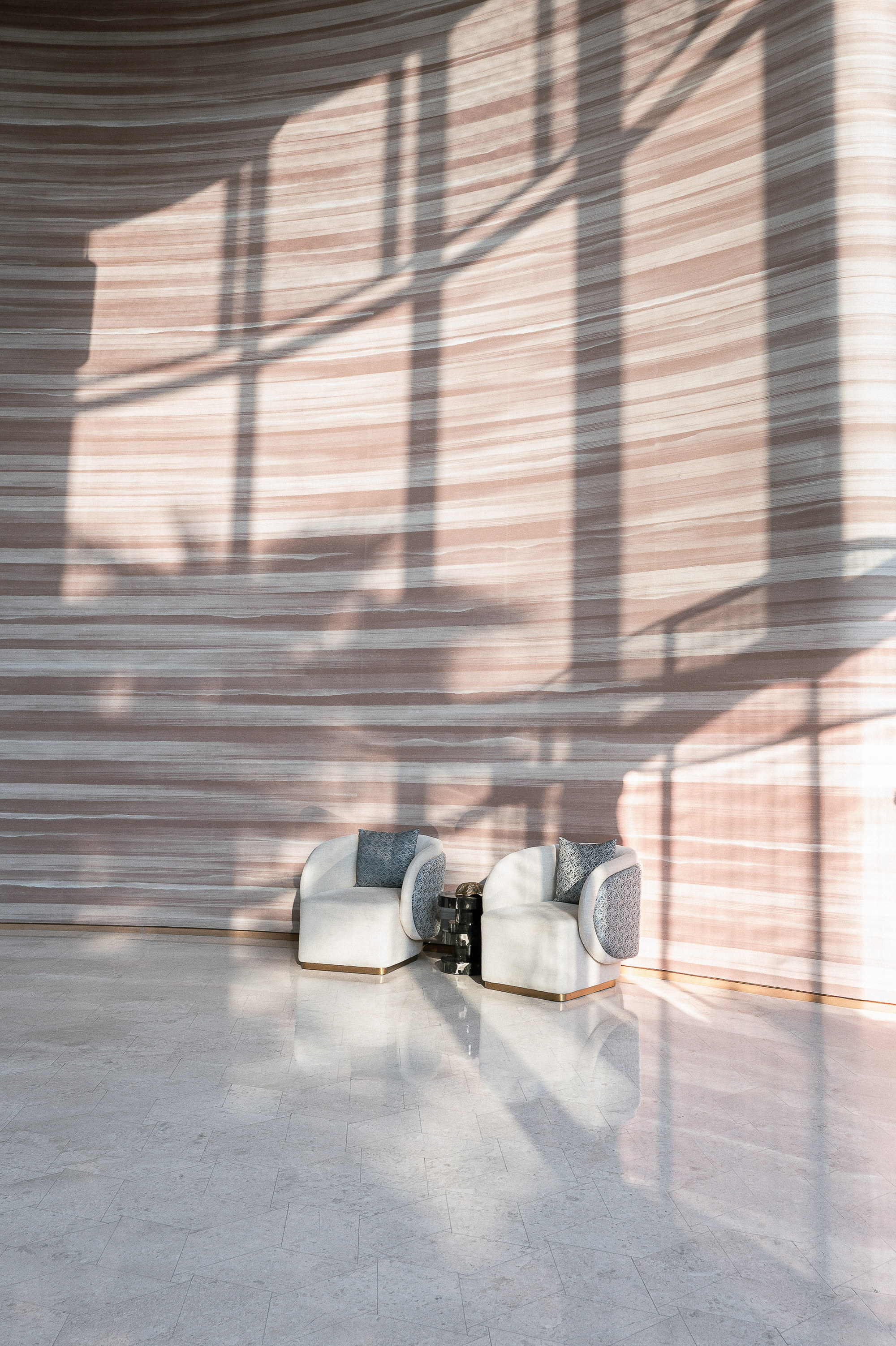 Two chairs against the striped stone, the window shadows laid across the wall