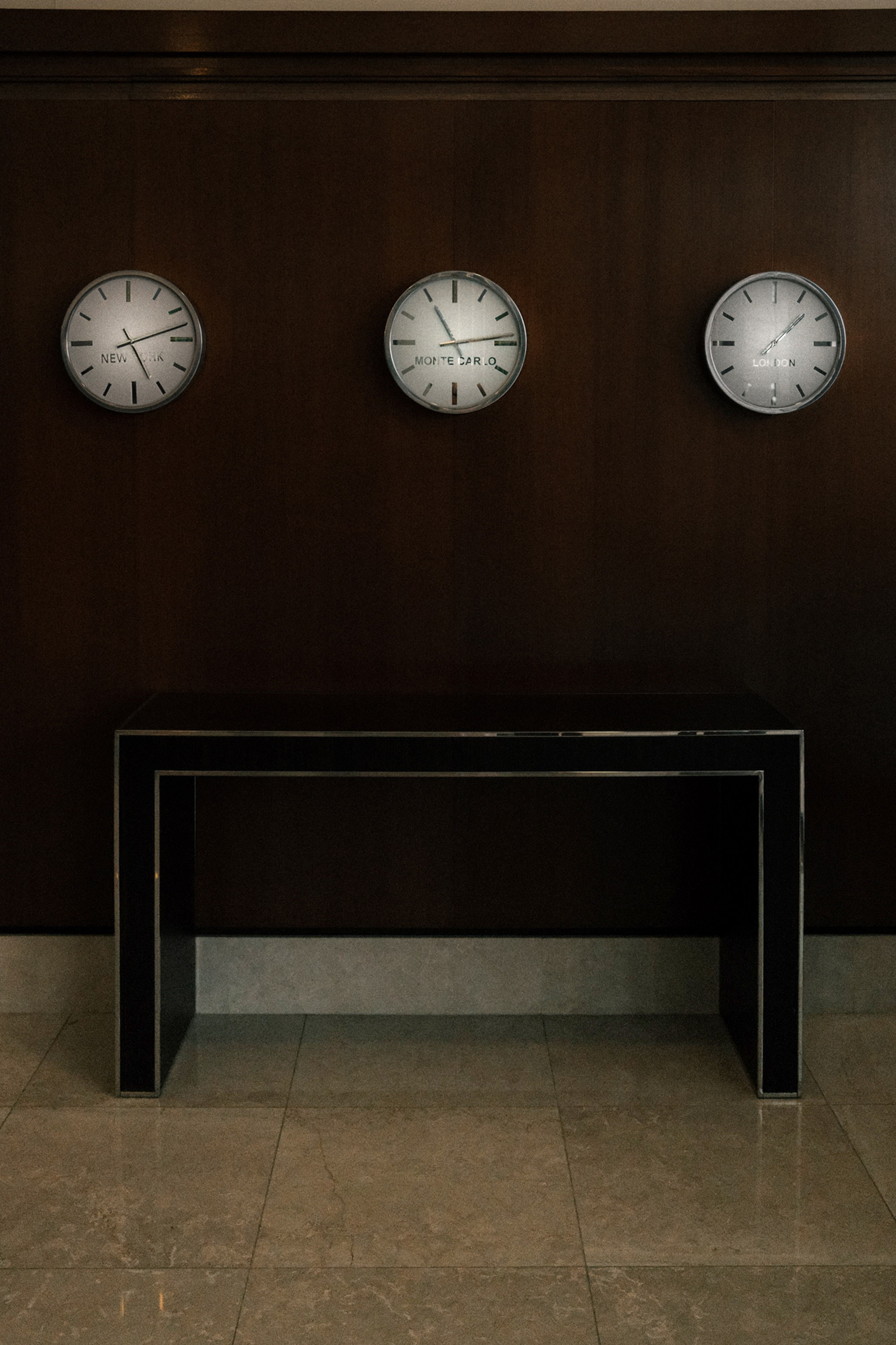 Three dials on dark panelling, New York and Monte Carlo and London, a console beneath