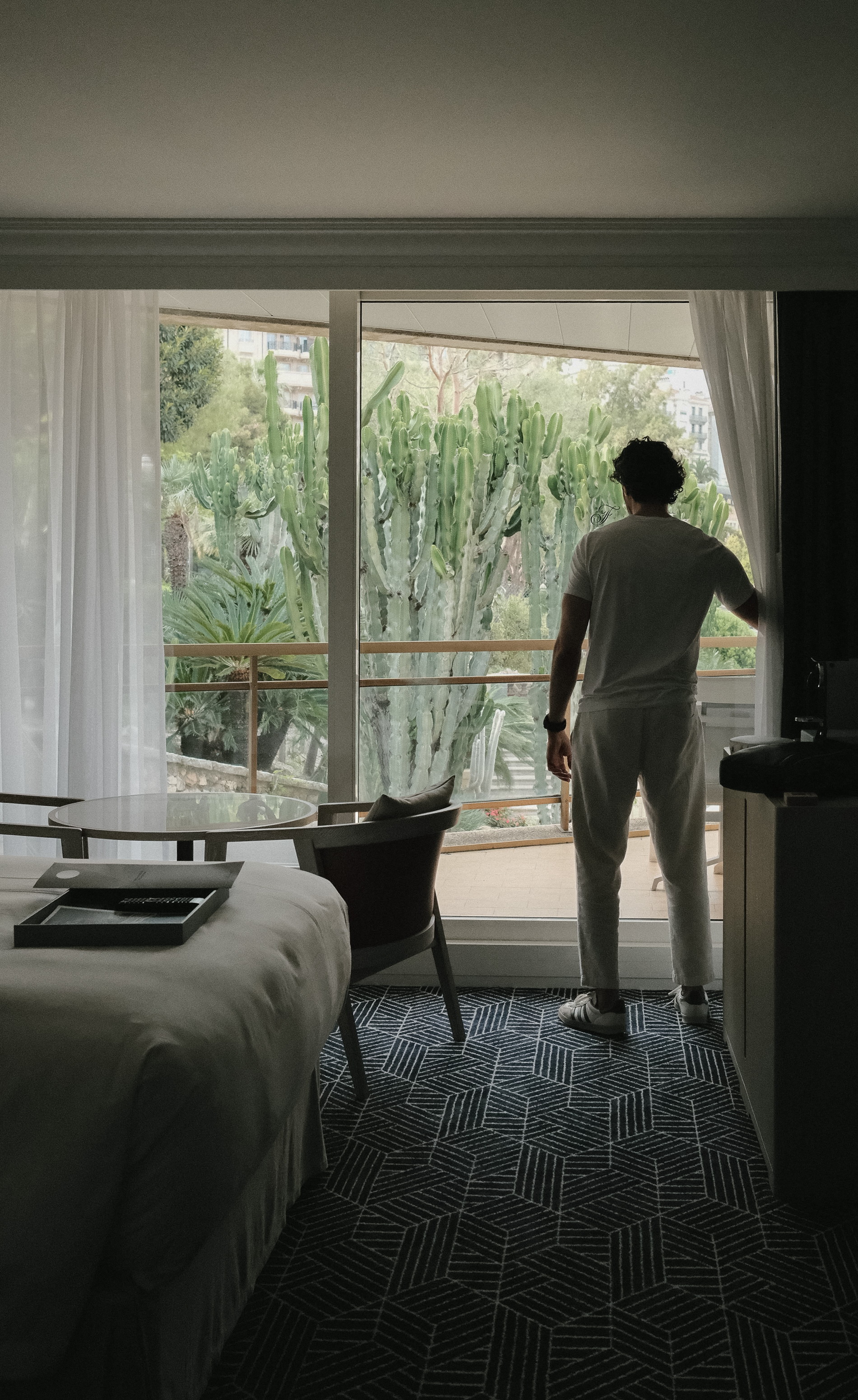A figure in white at the open window, the cacti standing outside, the house monogram on the glass